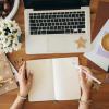 Person sitting at a desk with a journal open to a blank page.