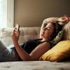 Student lying on the couch with headphones looking peacefully at her phone. 