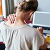 Girl rubbing her neck with discomfort while she works at a messy desk.