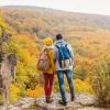 Two students bundled in sweaters standing on a hilltop overlooking colorful fall foliage.