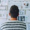 Student staring at a wall full of sticky notes and other pages of work.