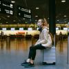 Young woman sitting on her luggage in an airport terminal.