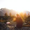 Girl sitting with her legs tucked in on a rock overlooking a mountain and sunset.