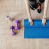 Person rolling up a yoga mat on the floor next to a water bottle and two dumbbells.