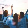 Photo of friends enjoying the sunset together with their hands raised high.