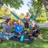 Photo of a group of students sitting on a lawn with a hammock smiling and chatting together.