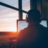 Students sits at his computer with headphones on as the sun sets in the window.