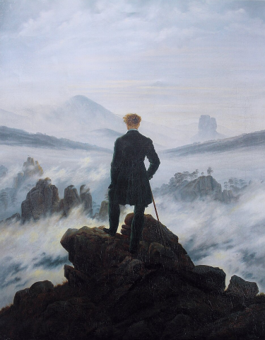 A man stands on a rock, turned away from the viewer towards fog