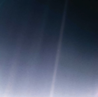 A mostly empty image of blue with a small speck in a ray of light