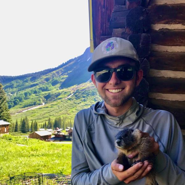 Austin Nash holds a marmot with mountains in the background