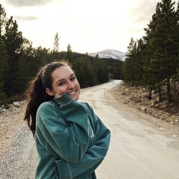 Ava Begun stands in front of a dirt road with trees in the background.