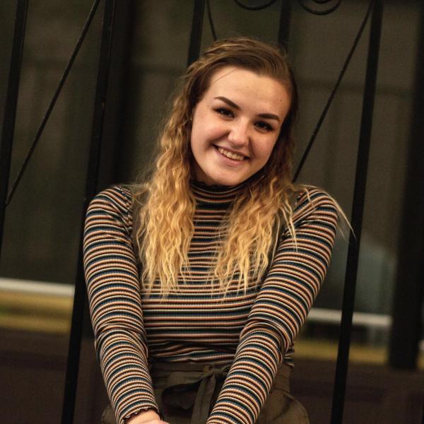 Darcy Brander sits in front of a metal fence.