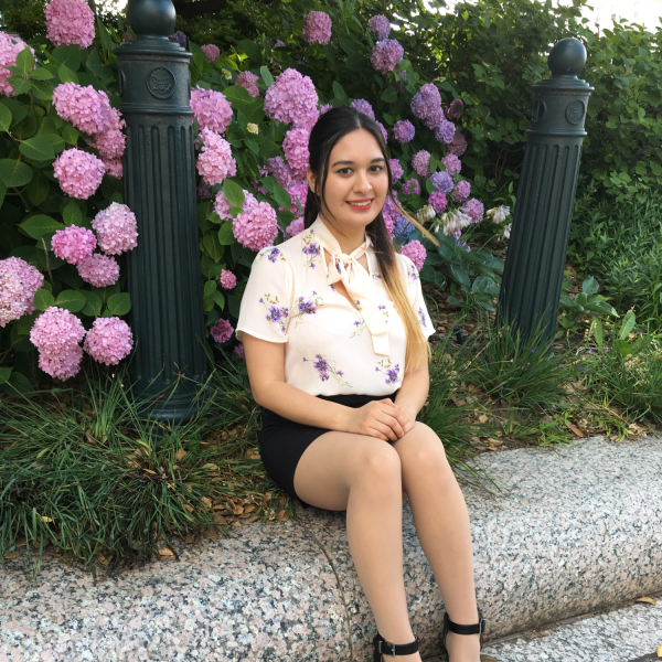 Lizzy Corona Jimenez sits in front of a flower bush.