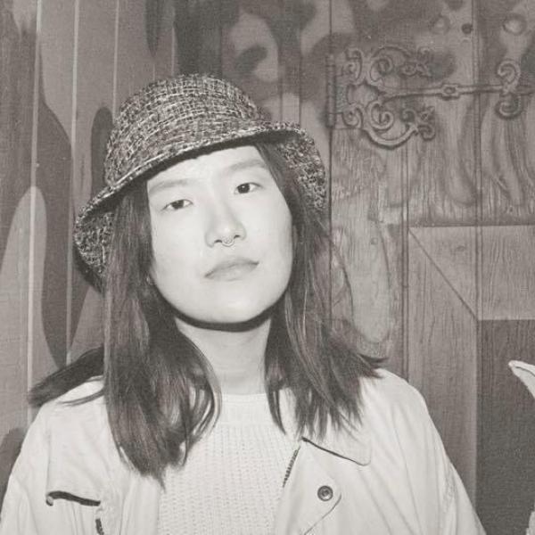 Shay Ding stands in front of a wooden wall. 