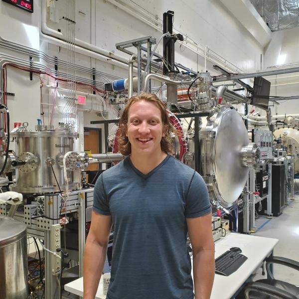 Alex Doner stands in front of equipment in a lab.