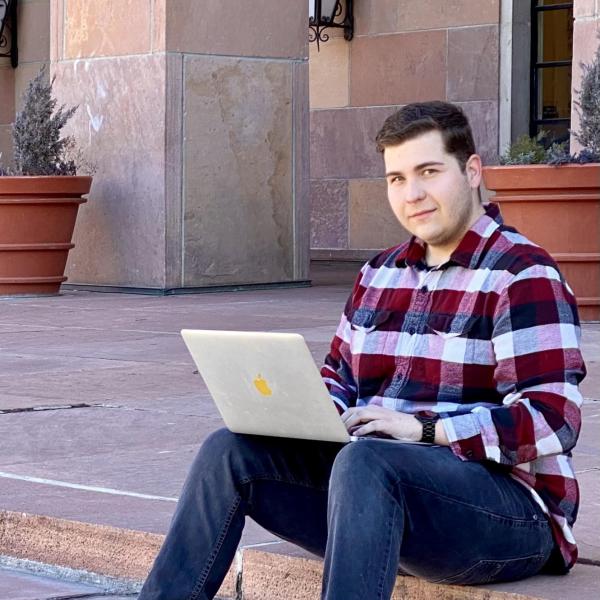 Zachary Girard sits in front of Norlin Library holding a laptop.