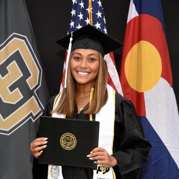 Sara Hauf stands in front of flags holding a certificate folder.