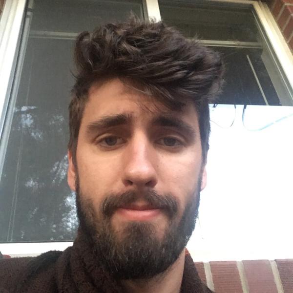 Jarrod Reilly leans against a brick wall with a window behind him