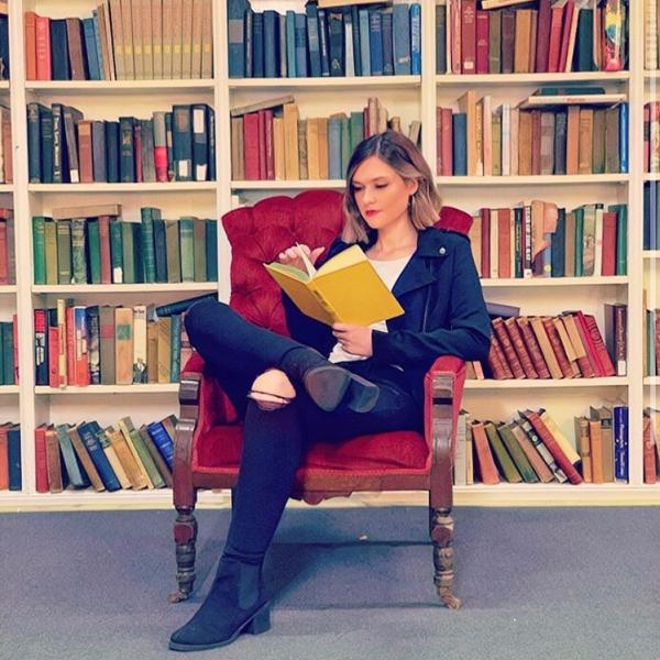 Katie Plain sits in an armchair in a roomful of books