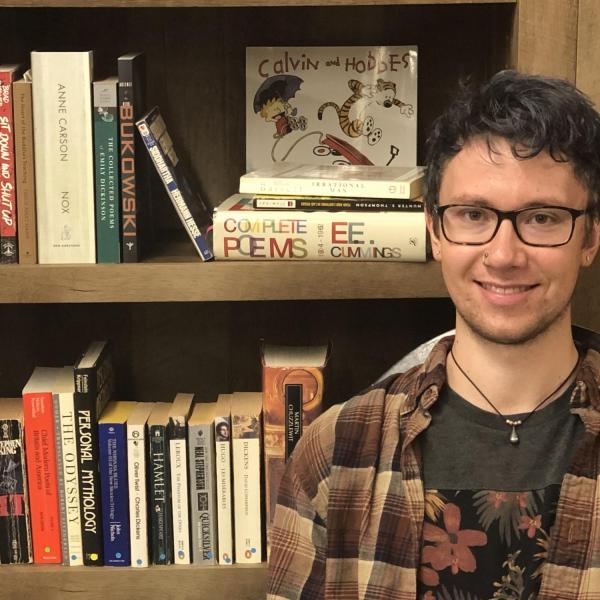 Landin Chesne smiles in front of a bookcase featuring E. E. Cummings and Calvin and Hobbes