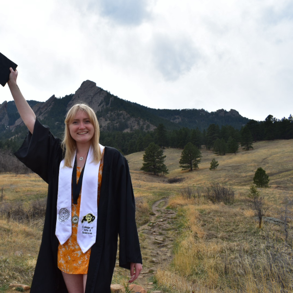 McKenzie Larson standing in front of mountains holding her graduation cap in her hand