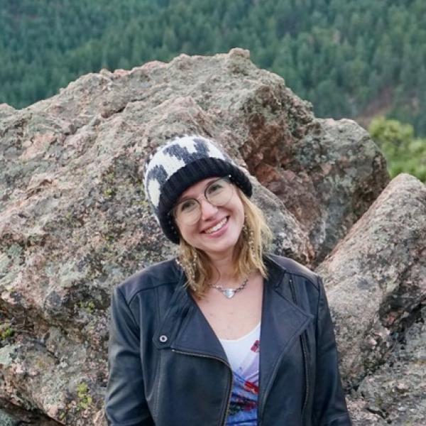 Moriah Major smiles in front of a boulder in the mountains