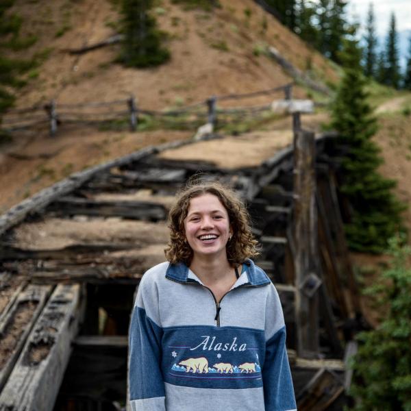 Pat Todd smiles in front of a dilapidated bridge in the mountains