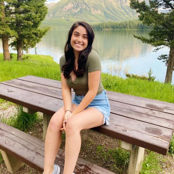 Ariana Squire sits on a picnic table in front of mountains.