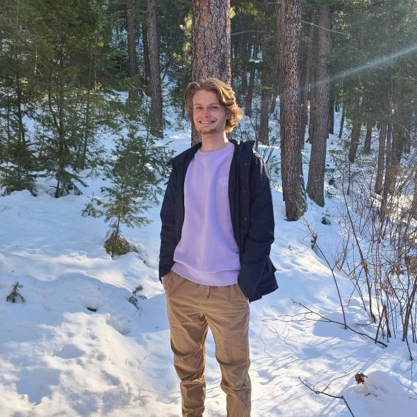 Kyle Sterns stands in front of trees with snow covering the ground around.