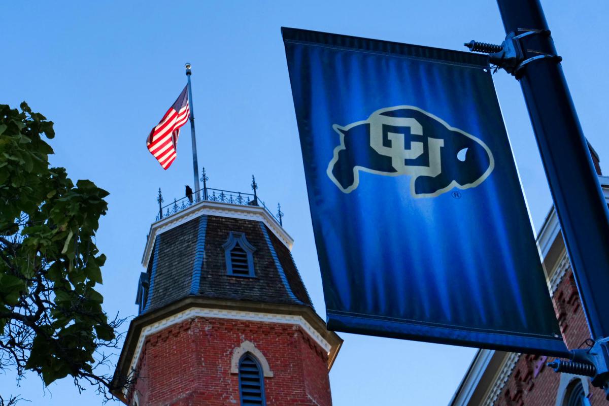 CU Buffalo flag in the foreground, with the top of Old Main behind it.