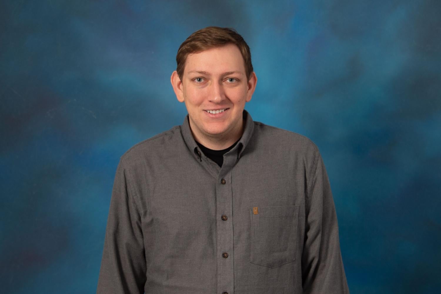 Jeffrey wearing a grey button-down shirt and smiling