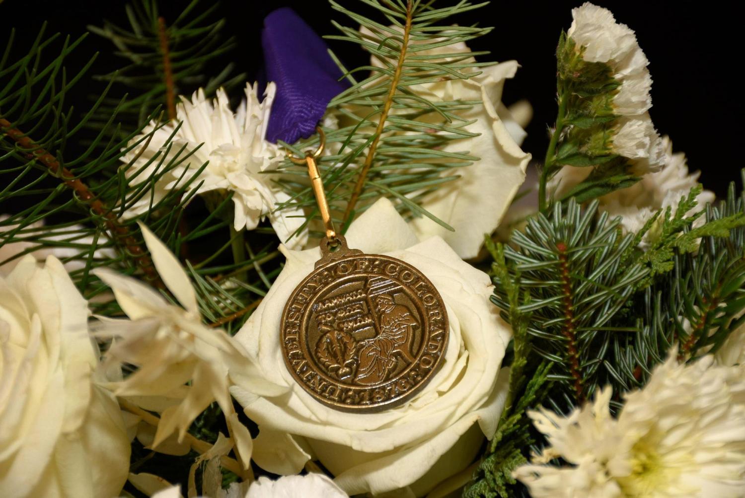 A close-up of the summa cum laude medal on a bed of flowers and pine tree branches