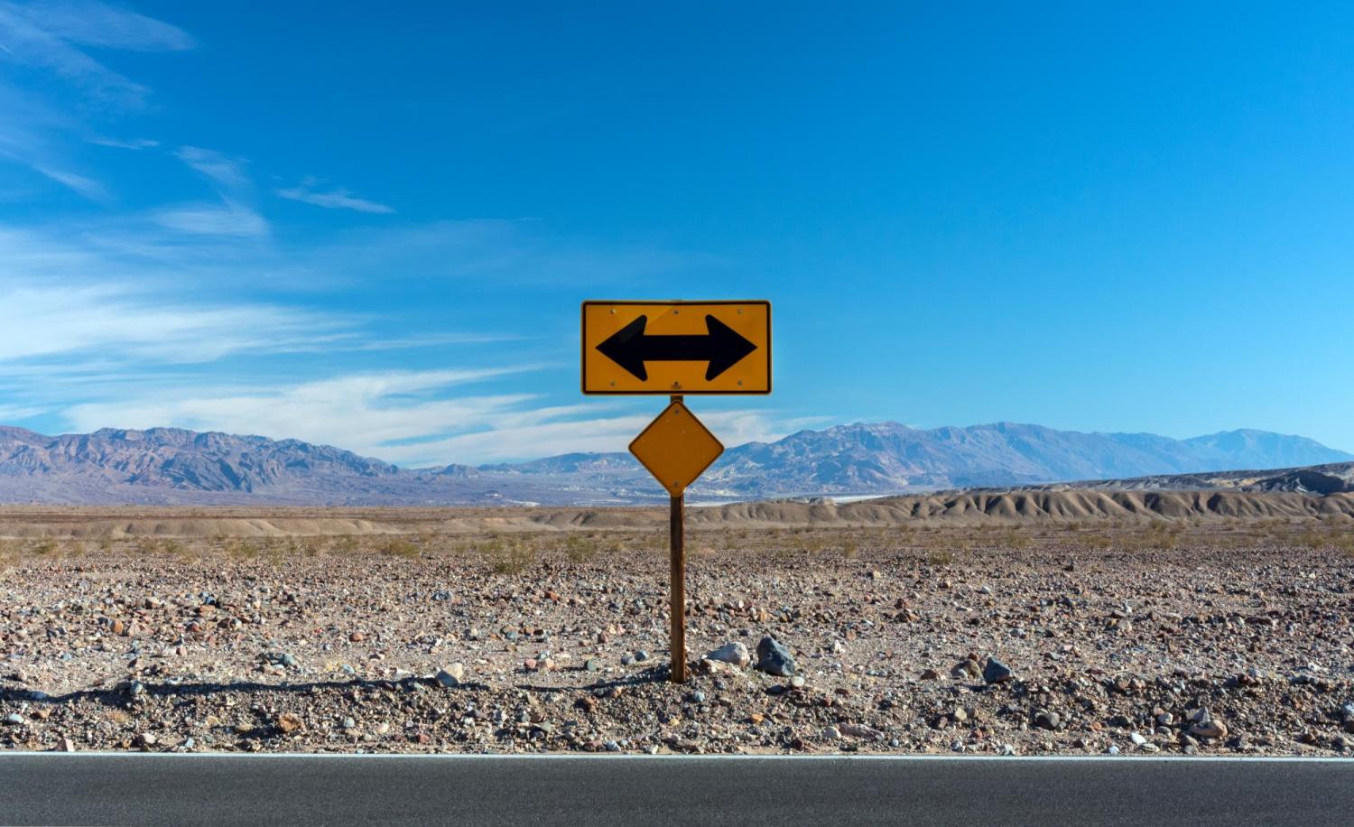 Road sign points left and right, with desert in the foreground and mountains in the background