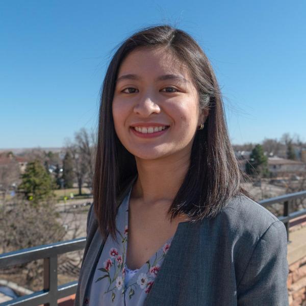 Alaynah Penalosa stands on a balcony with blue skies and trees in the background