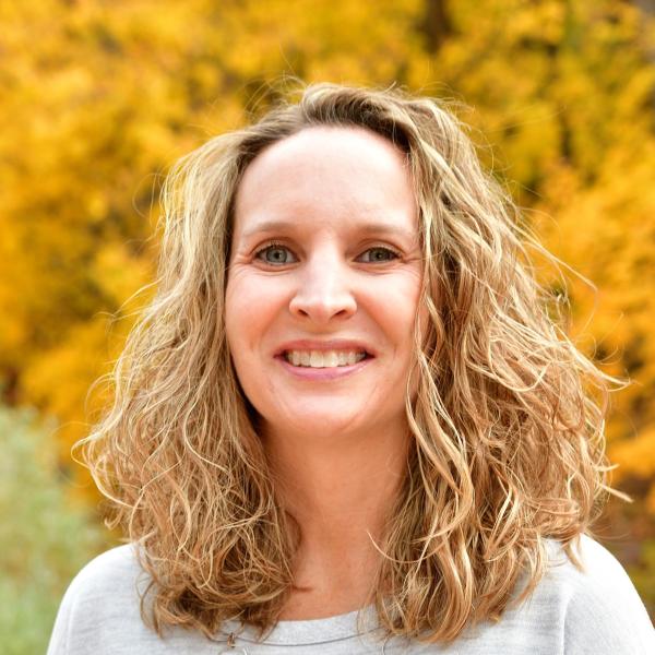 Ali Hatch smiles in front of a tree with golden fall leaves