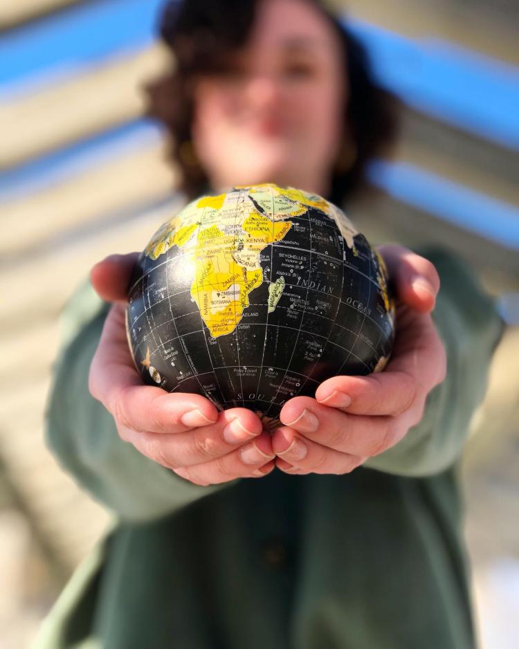 Out-of-focus person in the background with their hands outstretched holding a globe in the foreground