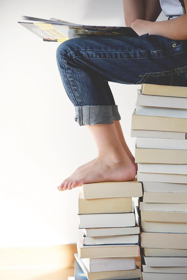 Girl sitting on a stack of books reading