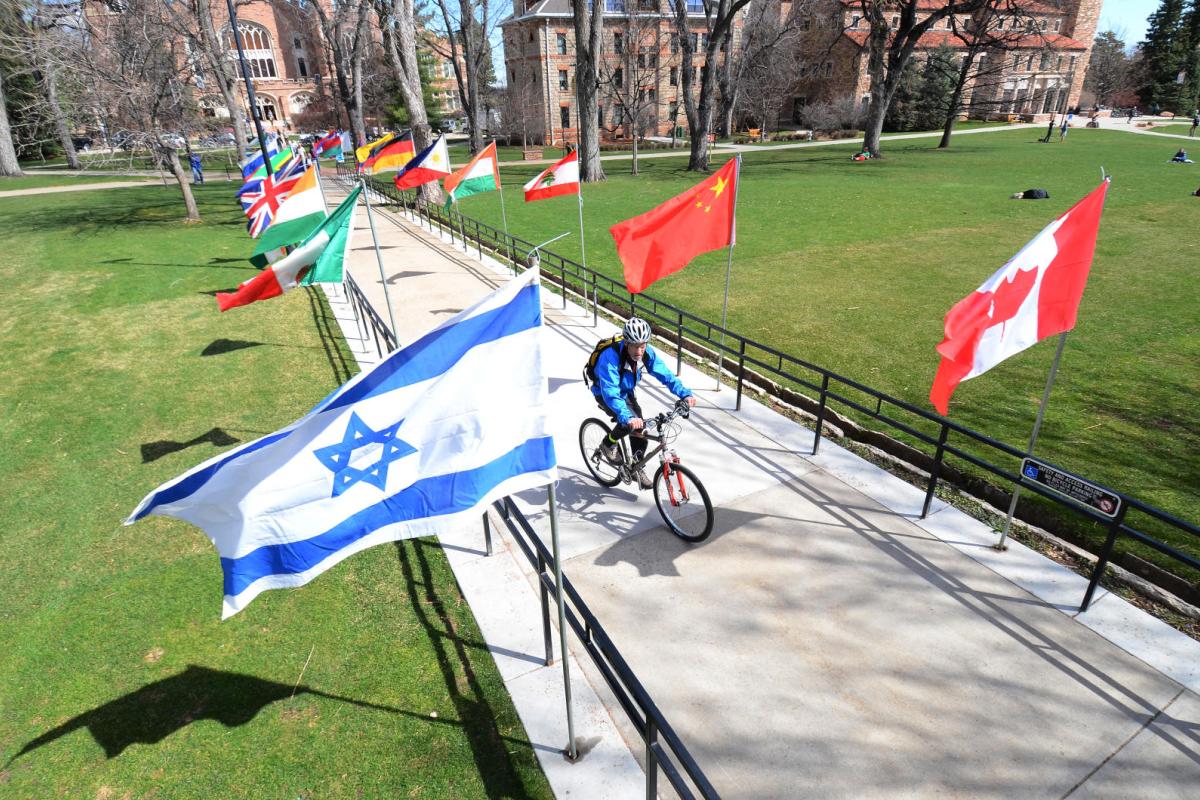 person riding bike on CU campus with various country flags