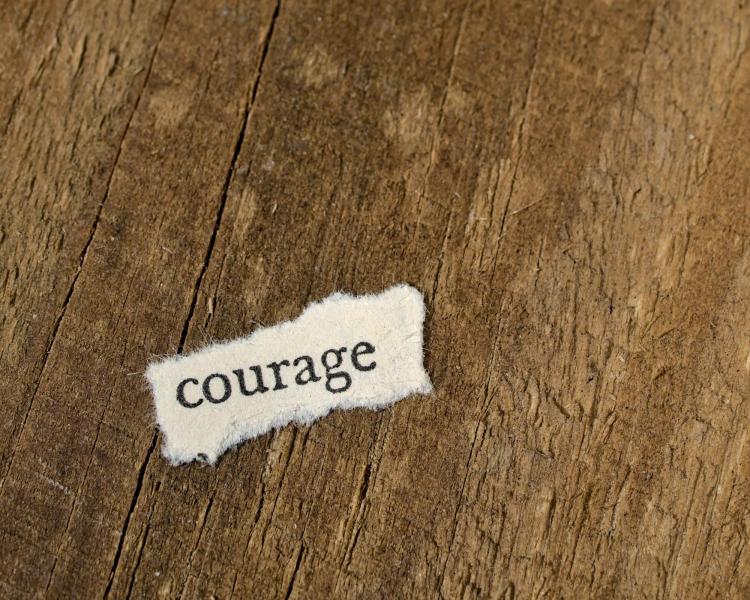 wood background with piece of paper that says courage