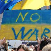 woman holding sign with ukraine flag colors and "no war" written on it. 