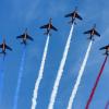 9 jet airplanes flying in arrow formation trailing blue, white and red contrails