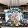 large globe hanging from the ceiling in a glass staircase area. 