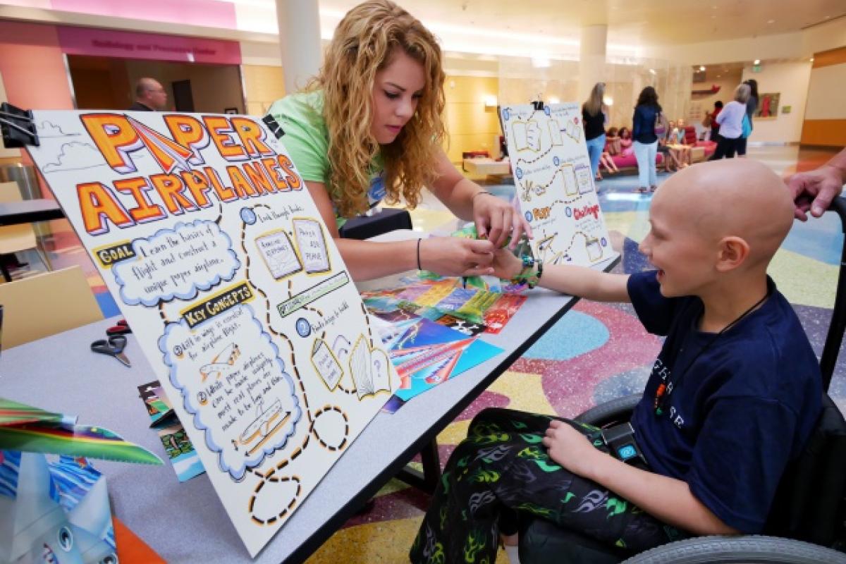 Student helping young patient at a paper airplane booth