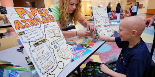 Student helping young patient at a paper airplane booth