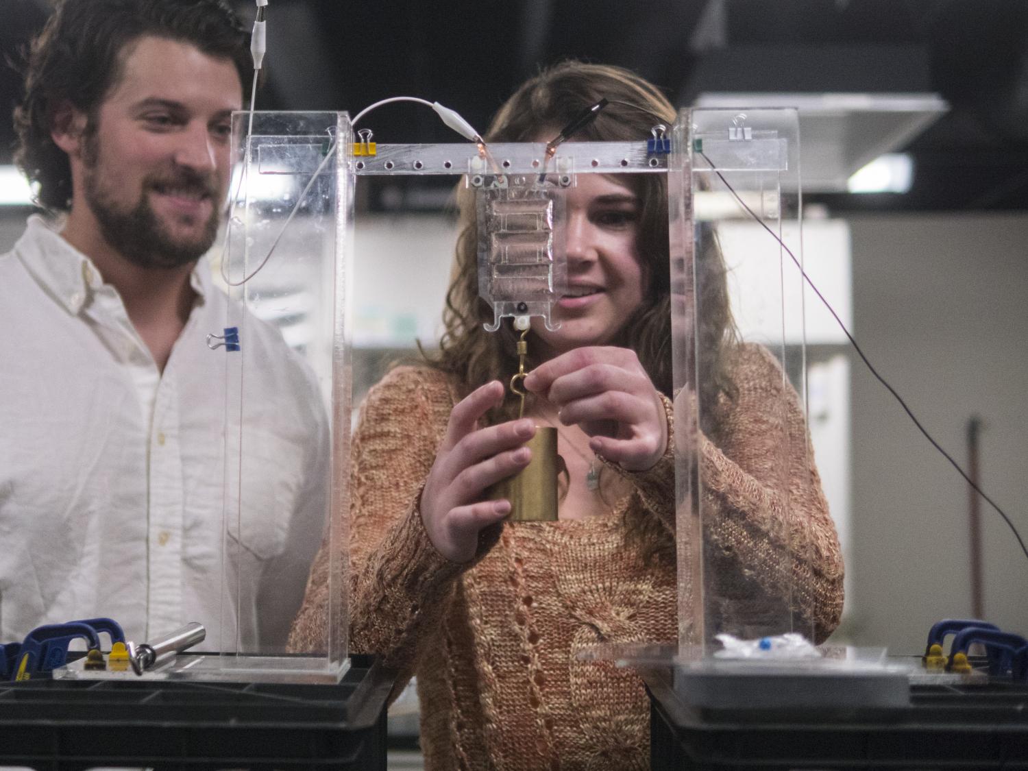 A student experimenting with a weight hanging from a mechanical device. Her professor is encouraging.