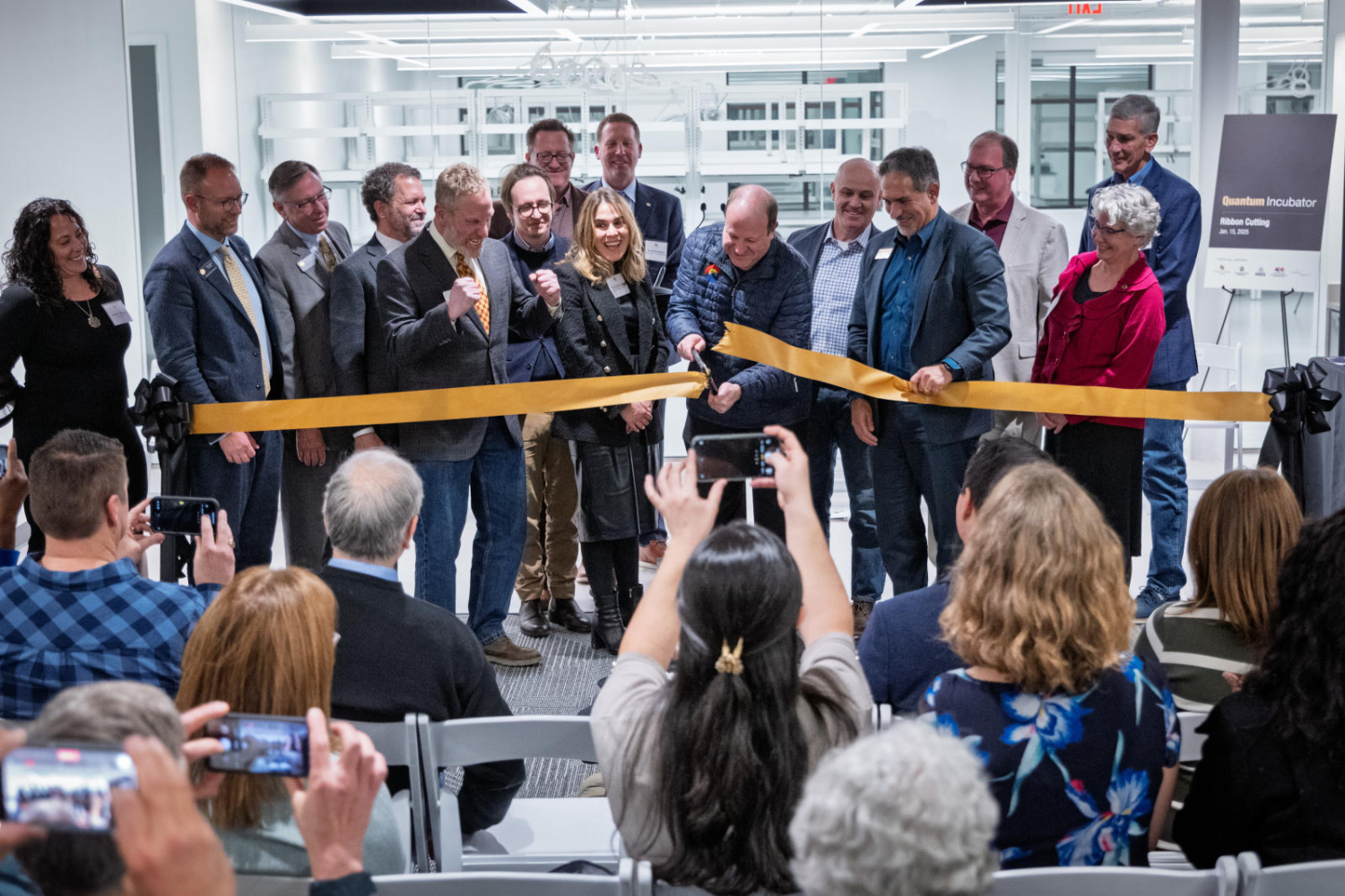 Platform guests and dignitaries watch Gov. Jared Polis cut a ribbon to celebrate the opening of the Quantum Incubator site