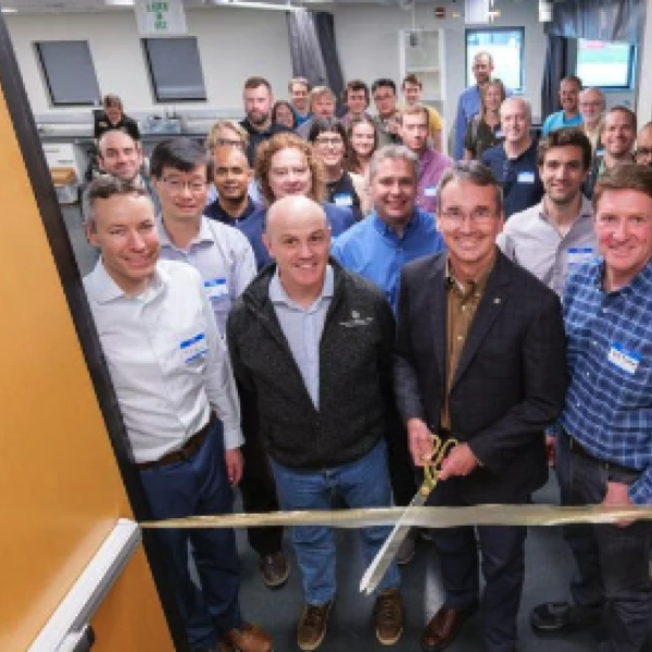 A group of predominantly white men stand at a ribbon cutting in the entrance of a laboratory