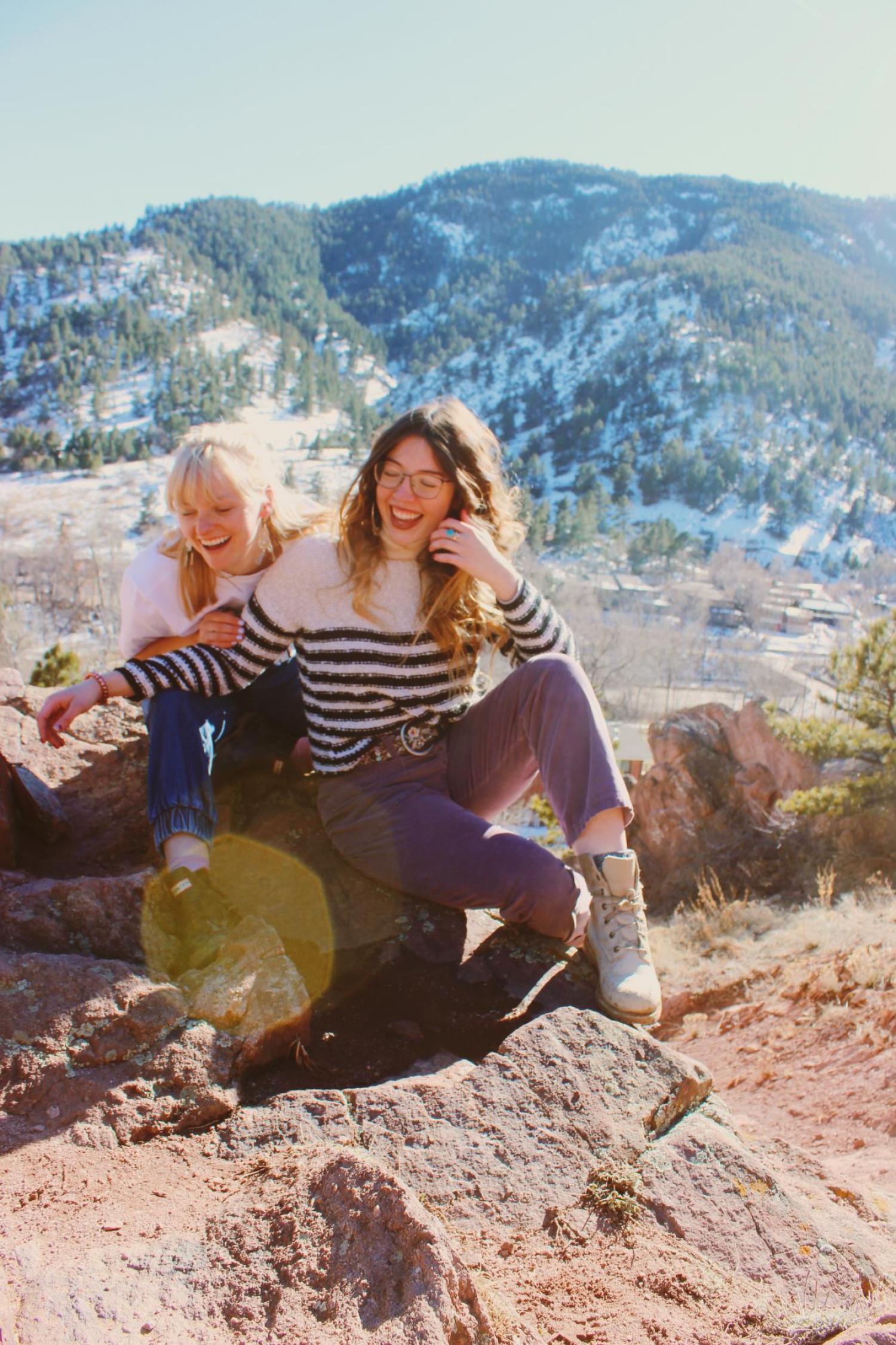 two females sitting on a rock laughing