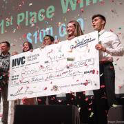 A diverse team of students stands on stage with their giant prize-winning check, the air is full of confetti, their joy is infectious