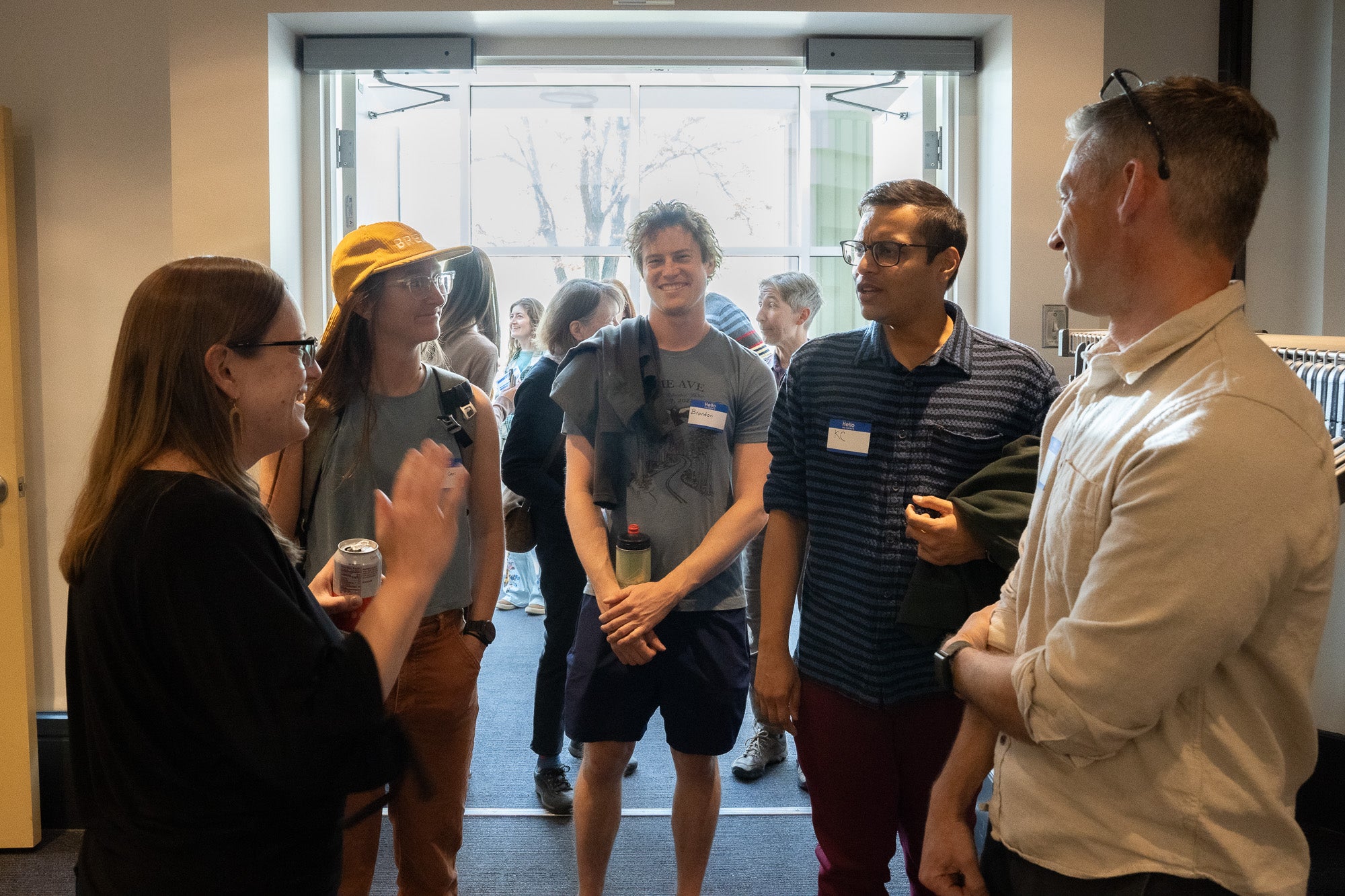 People in casual to business casual clothes smile and chat in front of a sunny doorway
